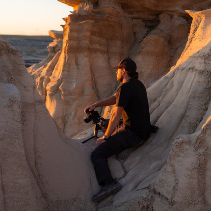 Tony sitting on a sandstone formation with a camera, surrounded by natural rock formations.