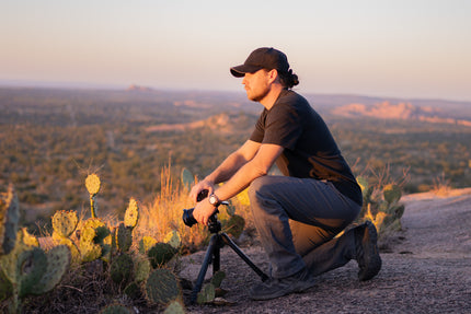 Tony setting up a camera on a tripod in a desert landscape at sunset.